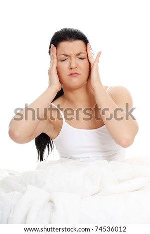 Young caucasian female sitting on bed. She have terrible headache (illness or hangover). Isolated on white