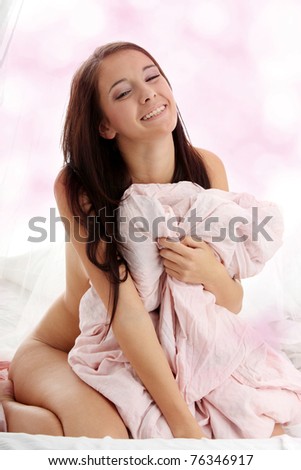 Young brunette sitting on the bed and covering her naked body with pink bed sheet