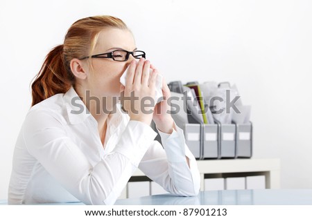 Caucasian businesswoman in glasses sneezing in the office.