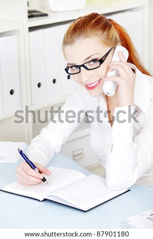 Beautiful caucasian girl in glasses smiling and answering the phone in the office.