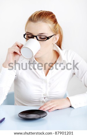 Sitting woman in glasses drinking coffee in the office.