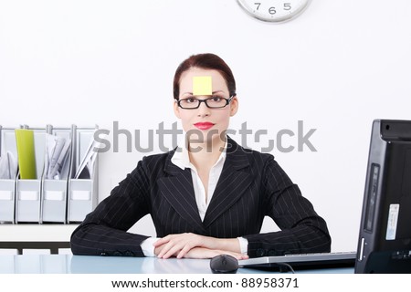 Pretty caucasian businesswoman sitting in the office with post it note on her forehead.