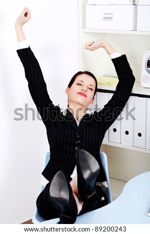 Beautiful caucasian businesswoman with legs laying on the desk stretching in the office.