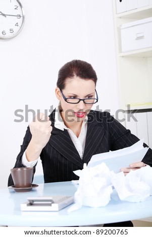 Pretty caucasian angry businesswoman reading files near crumpled files and sitting in the office.