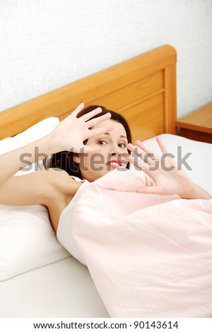 Closeup of a terrified woman defensing with her hands in bed.