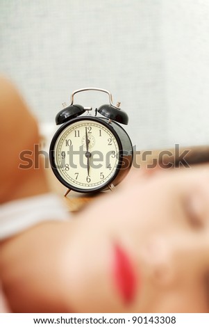 Face closeup of a young beautiful woman sleeping in bed, with a black alarm clock in the background - zoom in on the alarm clock.