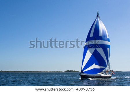 A yacht sails on lake Grevelingen (Netherlands) with a huge blue-white spinnaker on a bright summer day