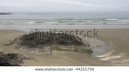 Ocean waves roll ashore on a deserted beach with sand and rocks