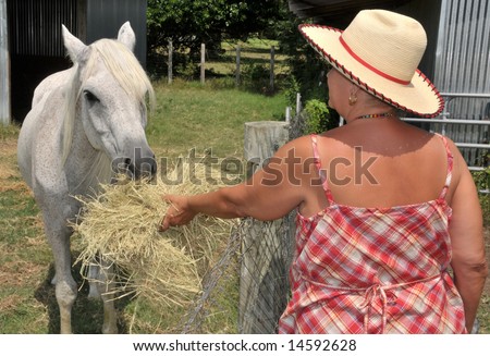 A senior woman on a farm feeds a white horse
