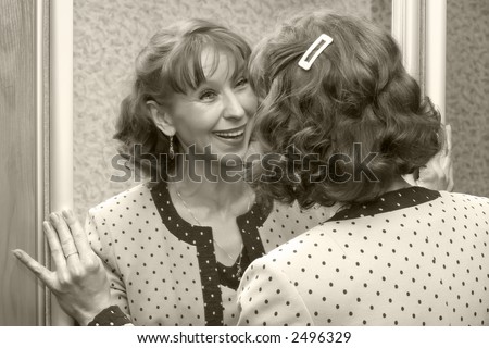 Attractive woman of average years cheerfully looks at the reflection in a mirror