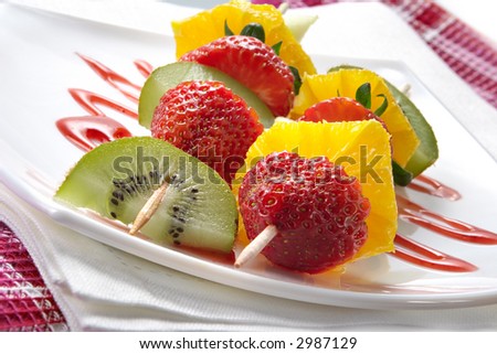 Fruit allsorts on skewers served atop of a plate decorated by strawberry jam