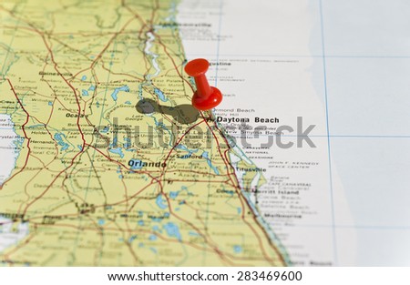 Daytona Beach marked on map with red pushpin. Selective focus on the word Daytona Beach and the pushpin. Pin is in an angle and casts some shadow to the left.