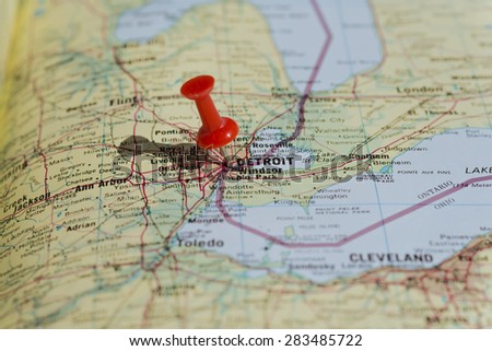 Detroit marked on map with red pushpin. Selective focus on the word Detroit and the pushpin. Pin is in an angle and casts some shadow to the left.