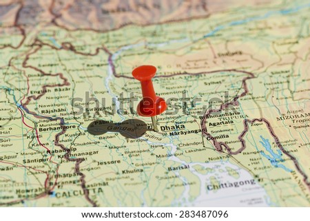 Dhaka marked on map with red pushpin. Selective focus on the word Dhaka and the pushpin. Pin is in an angle and casts some shadow to the left.