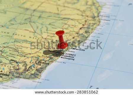 Sydney marked on map with red pushpin. Selective focus on the word Sydney and the bottom of pushpin. Pin is in an angle and casts shadow to the left.