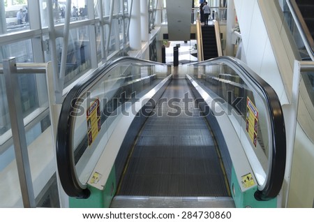 Image of a moving walkway or inclined travellator at an airport. Nobody is using the moving walkway at the time of image taken. Glass side rails and black rubber handrails.