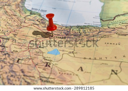 Tehran marked on map with red pushpin. Selective focus on the word Tehran and the pushpin. Pin is in an angle and casts some shadow to the left.