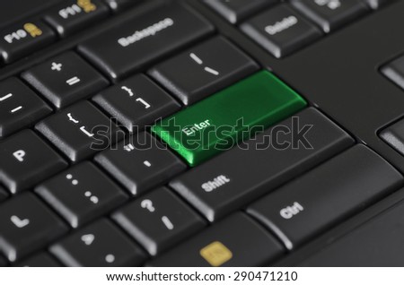 Close up shot of a computer keyboard in an angle with focus on green enter button. Keyboard is black with white and yellow letters on buttons.