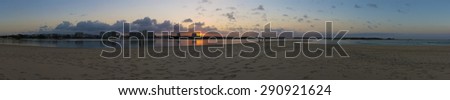 Panoramic image of Maroochydore taken from Cotton Tree. Foreground has sandy riverbank, mid-ground is Maroochy river and Maroochydore CBD highrise buildings. Sun is setting behind one of the buildings