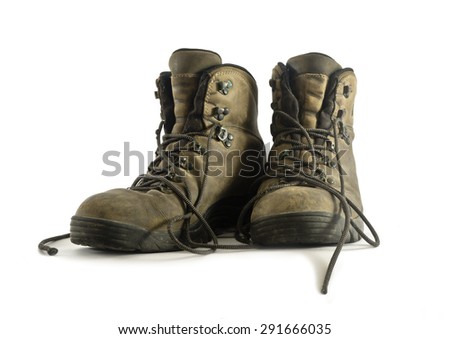 A pair of dirty worn hiking boots closeup on white background. Boots have grey leather upper and rubber soles. Shoelaces are loose. Image shows front view of boots with lacing, upper and tongue.