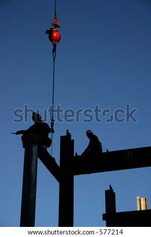 Image of two construction workers directing an i-beam into its final position. The red weight of the crane is the only color element in this image except for the sky. Image is not retouched.