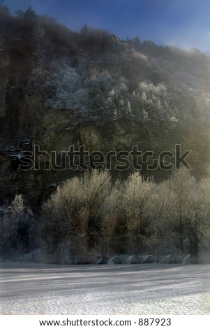 a rock face in the rising sun, snow-covered trees in the foreground. Slight fog enhances the atmosphere.