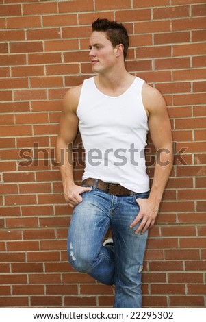 A handsome young male model leaning against a brick wall.