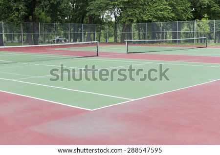 Empty Suburban Tennis Court In Park\
\
A view of a fenced in area in a park for two tennis courts.