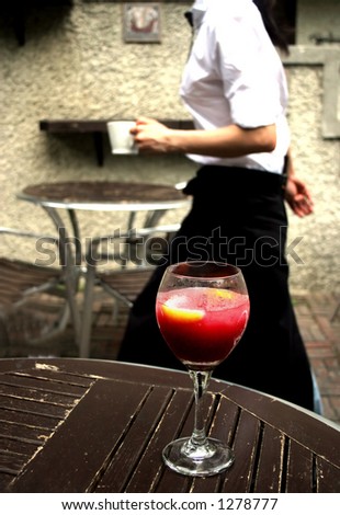 Busy waitress working in a city restaurant glides by a table with a glass of red wine