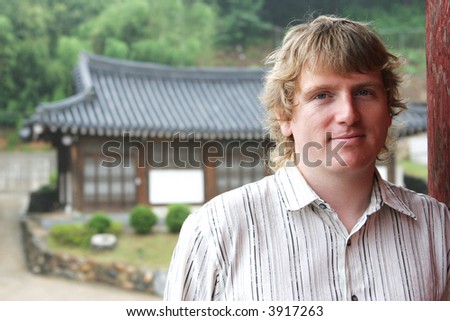 Blond man smiling with oriental buildings in the background - travel and tourism. NOTE: Light rain, not noise.