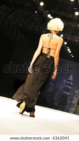 Blond model in a sexy dress walks down the catwalk during a fashion show.