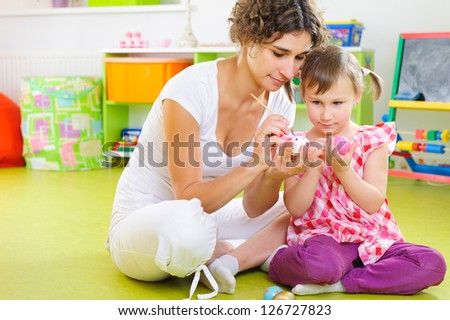 Young mother and daughter painting and decorating Easter eggs at home