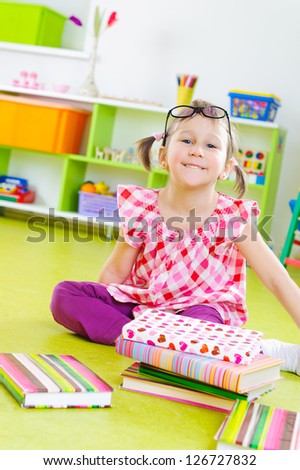 Funny little girl in glasses with books on floor