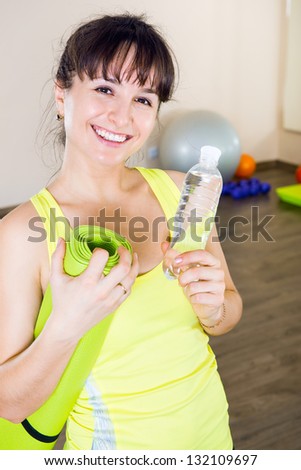 Young girl with a bottle of water and gym mat in sport club
