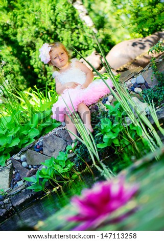 Cute little girl in ballerina tutu sitting at pond