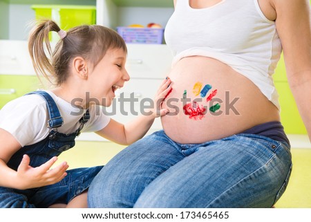 Cute little girl painting on pregnant mothers belly
