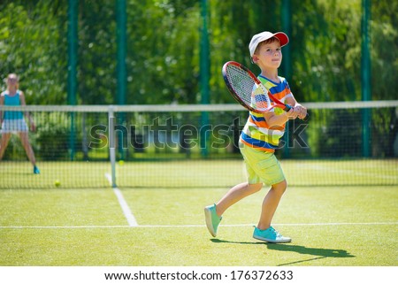 Little cute boy playing tennis on green court