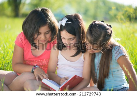 Three happy teen girls reading book at park
