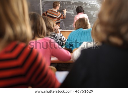 Male teacher and schoolgirl are near blackboard. Rear view