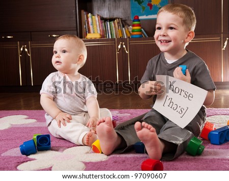 A boy aged three and a girl aged one are playing with blocks and cards with words