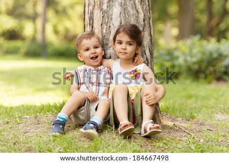 Little brother and sister expressing affection, sitting in nature and hugging.