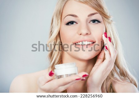Beautiful young woman applying skin moisturizer on her face