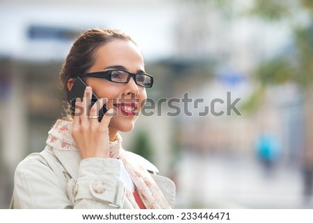 Beautiful young woman with glasses talking on the smart phone on the street