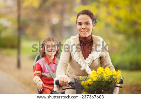 Mother riding a bicycle with her cute little daughter sitting on a back seat