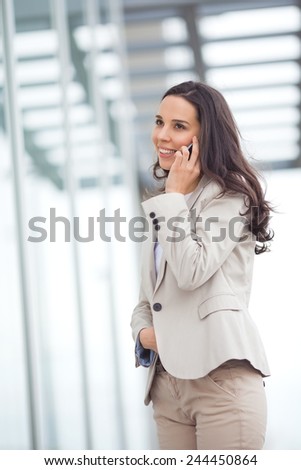 Smiling young business woman talking on the mobile phone in front of the office building.