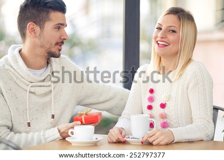 Romantic young man giving present to his girlfriend while sitting in a cafe