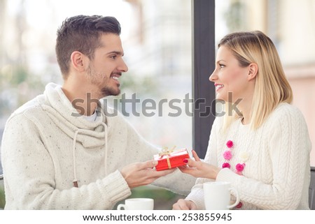 Romantic young man giving present to his girlfriend while sitting in a caffee