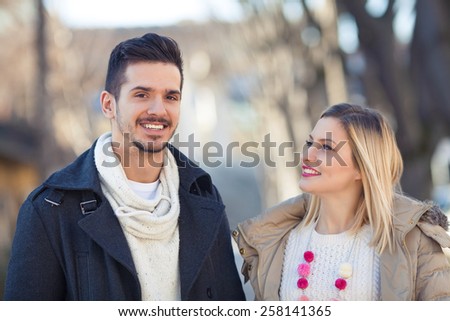 Portrait of happy young couple on the street. Young man is looking at camera, and girl is looking at her boyfriend.