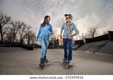 Young woman on rollerblades and young man on skateboard in a skate park