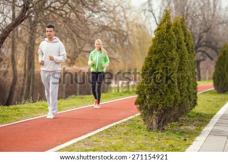 Two young people jogging on a running track in a park